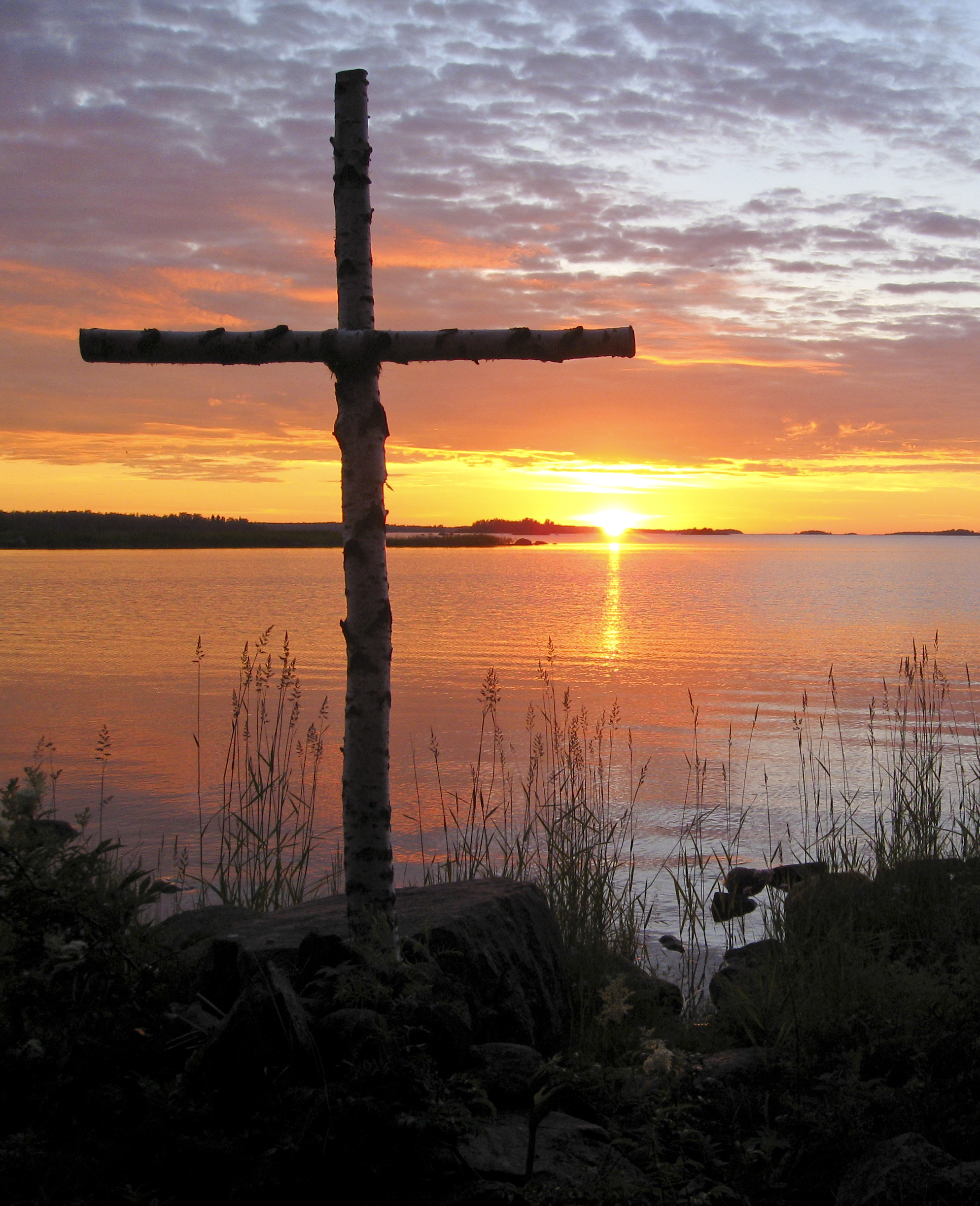 Ett kors som står på stranden i solnedgången.