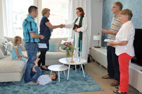 Familj och präst samlade i vardagsrum.