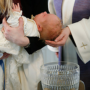 Baby hålls ovanför dopfunt, präst sätter vatten på huvudet