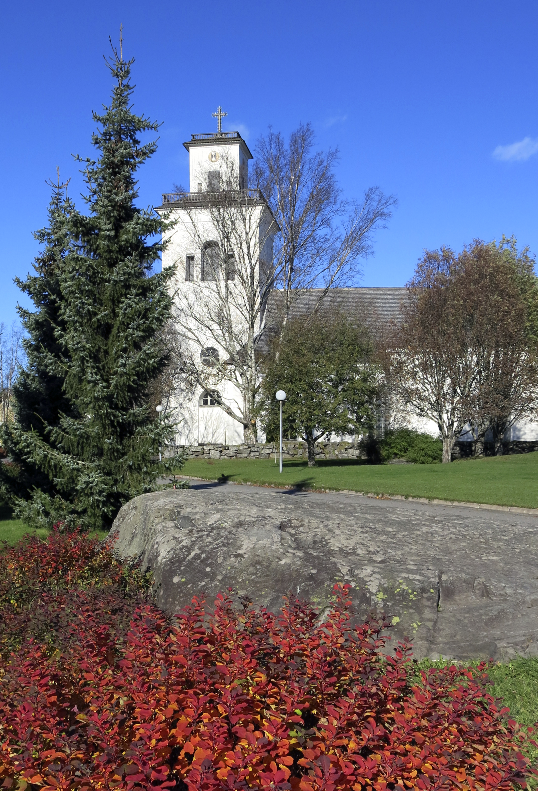 Karleby sockenkyrka i vit sten omgärdad av planteringar i höstfärger.