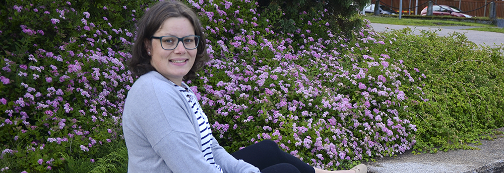 Carolina Myrskog sittande ute med blommor i bakgrunden.