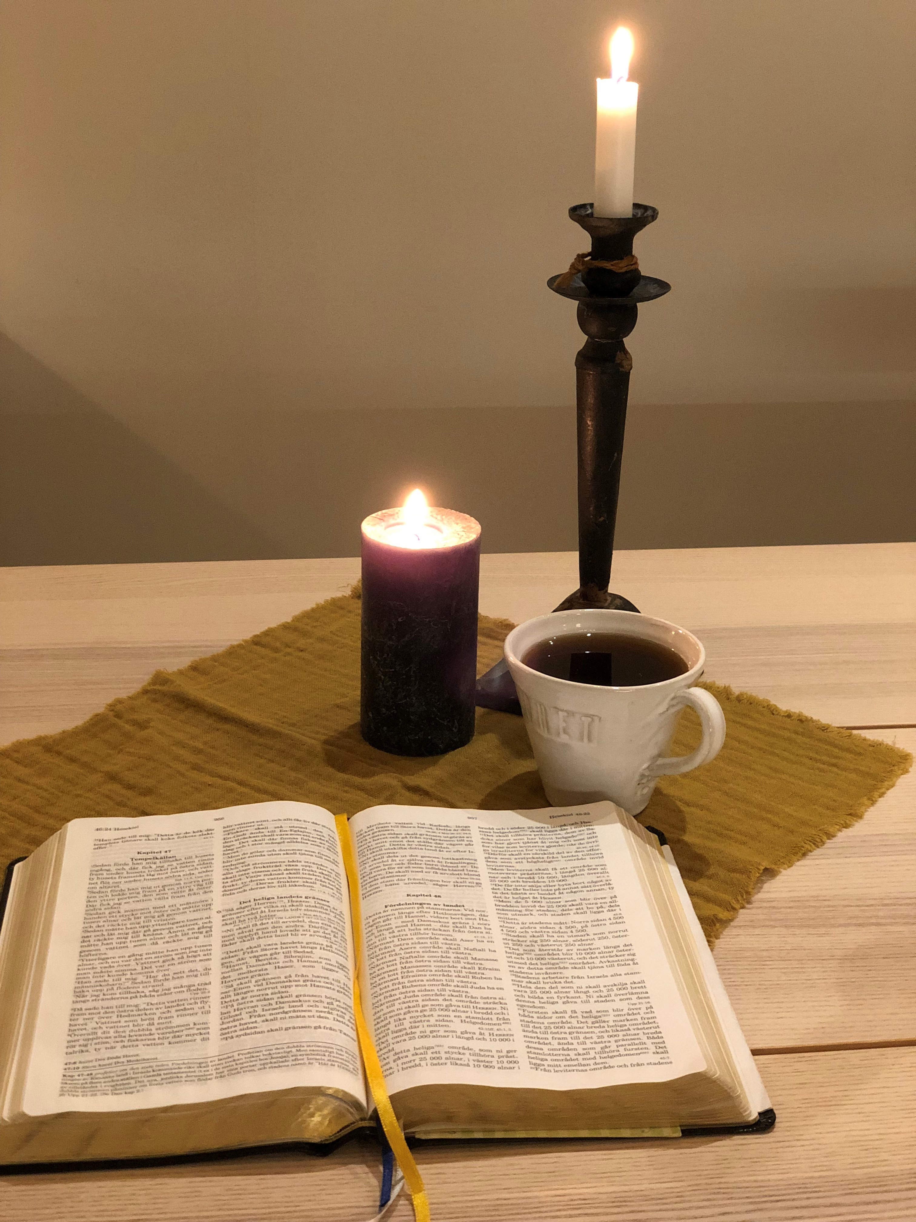 Öppen bibel på ett bord med ett ljus och en kopp kaffe bredvid.