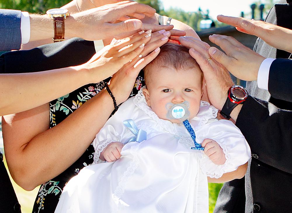 Baby döps och välsignas. Många händer hålls på barnets huvud.
