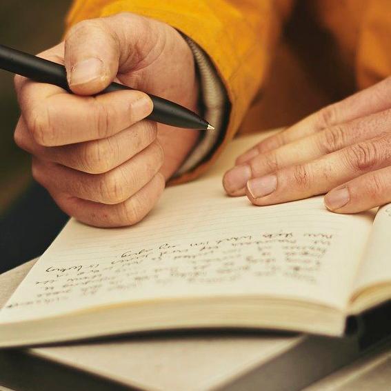 Öppen bok med hand som håller penna.