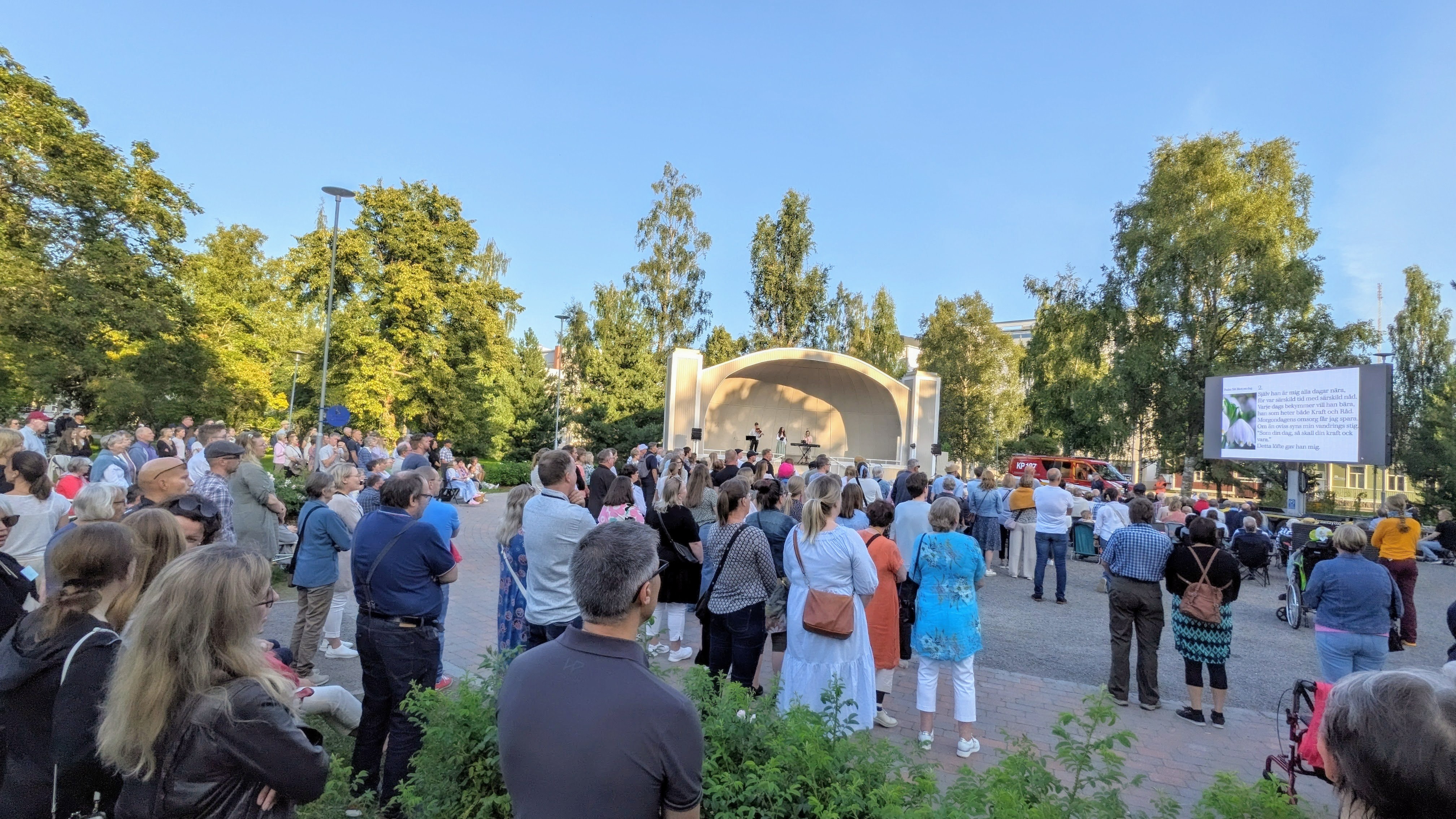 Människor i olika åldrar står i parken och sjunger.